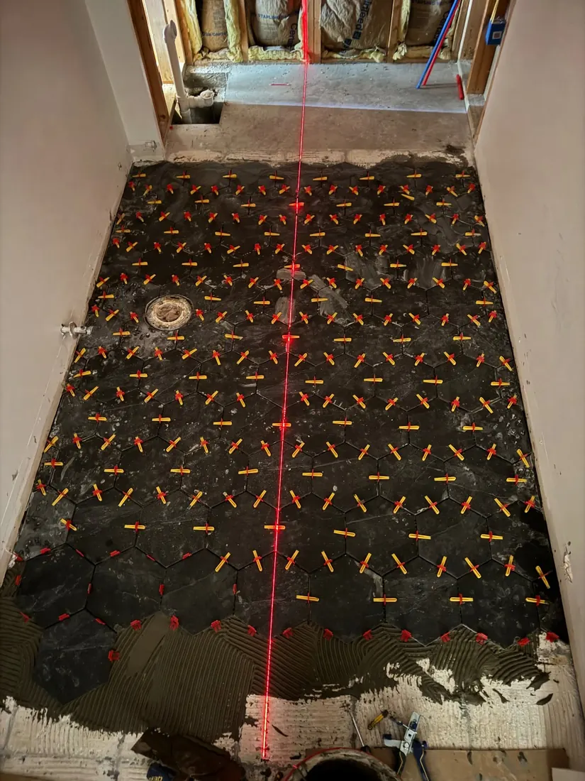 Black hexagonal bathroom floor tile being installed during Frontline Bathroom Project 2