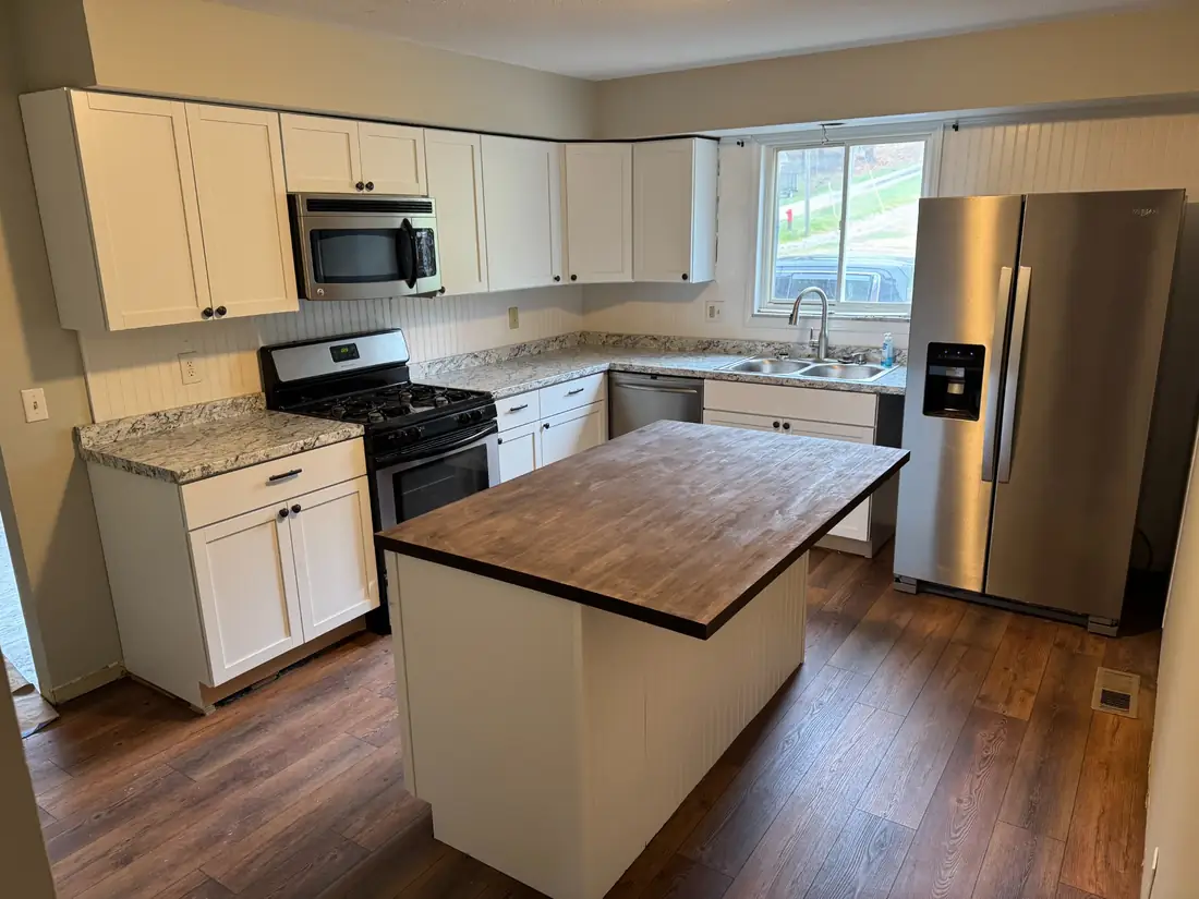 Completed Frontline kitchen remodel with white cabinets, updated counters, stainless appliances, wood-tone island, and new flooring