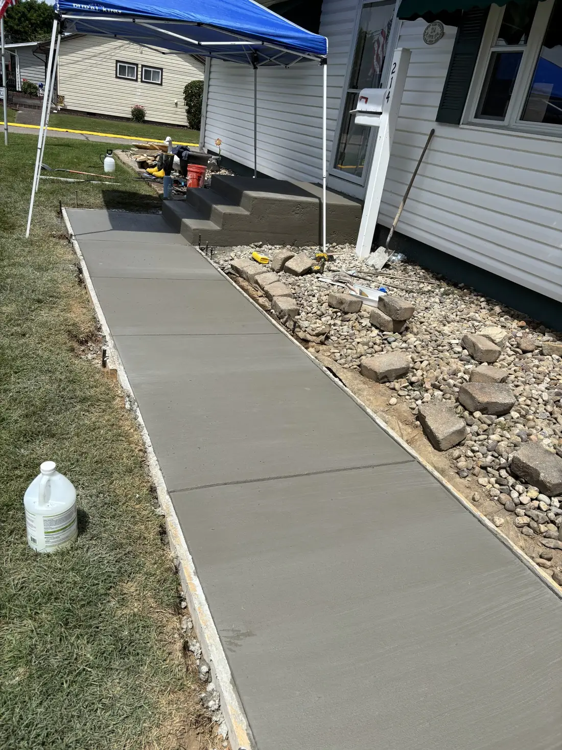 Freshly poured concrete walkway extending from the sidewalk toward the entry