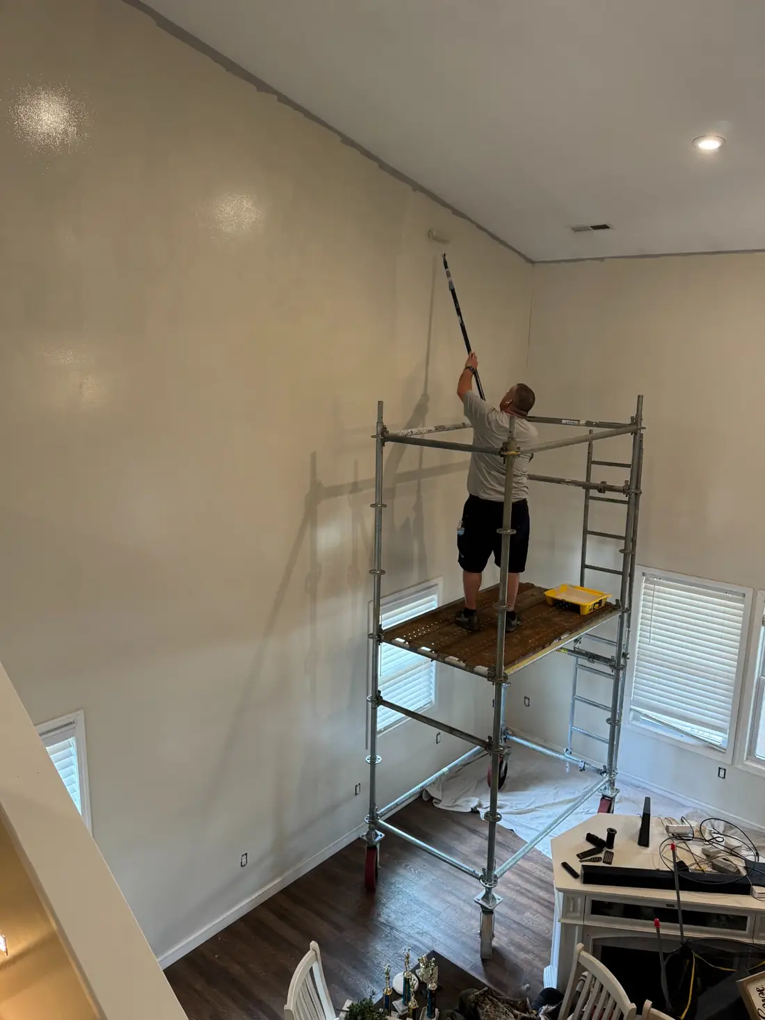 Frontline painter applying paint to a tall interior wall from mobile scaffold